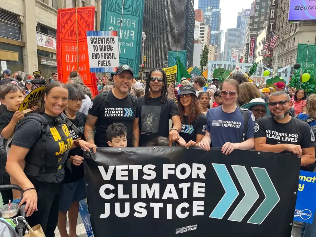 photo of multiple people standing behind a banner they are holding up that says "Vets For Climate Justice."